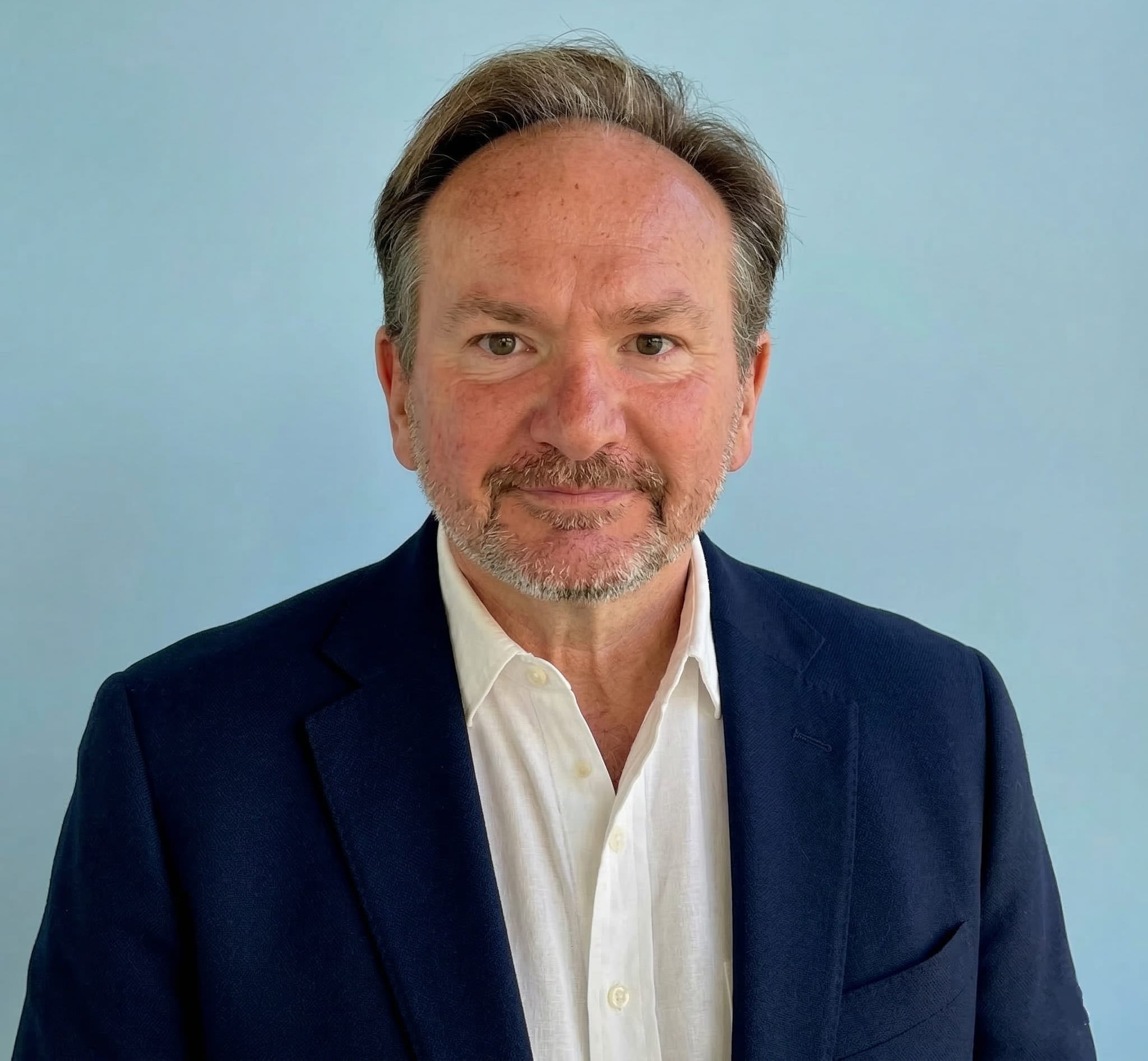 Photo of man in blazer, no tie.  Sky blue background.